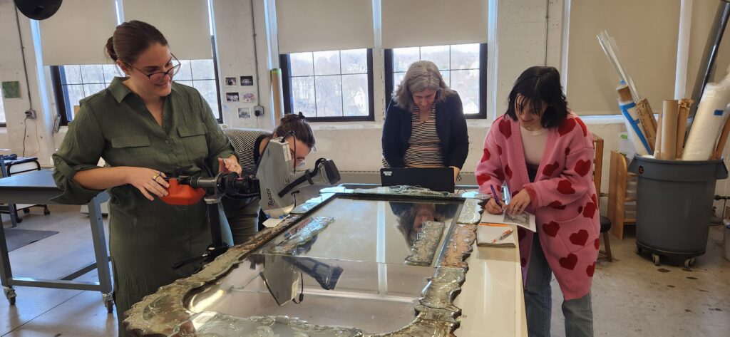 Several conservators stand around the looking glass flat on a table, examining it.