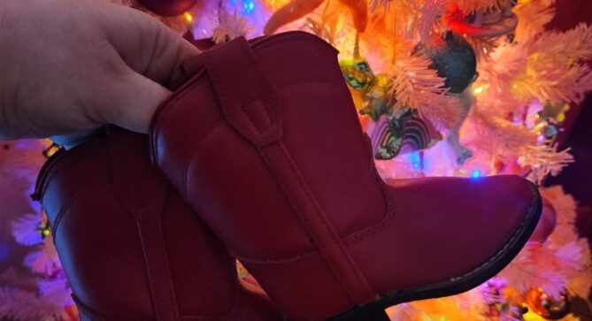 A pair of small, toddler sized red leather classic cowboy boots being held in the air