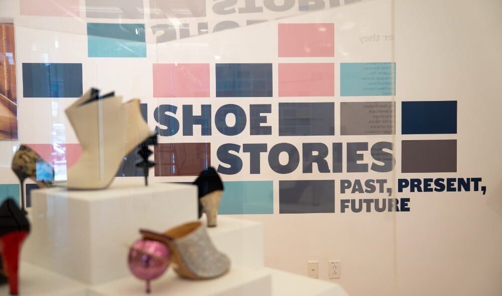 A photo from the Shoe Stories exhibition showing a selection of shoes and the signage. The signage reads: Show Stories - Past, Present, Future.
