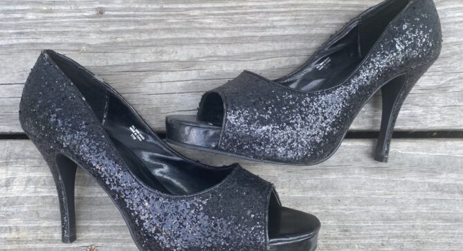 A pair of black sequin peep toe stilettos laying side by side on gray, weathered, wooden slats.