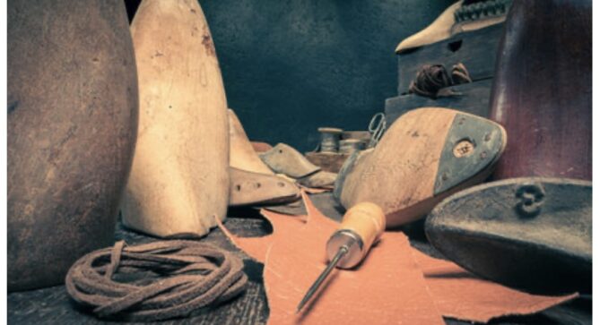 Shoemaking Tools, stock photo. A pointed awl sits at the center, surrounded by wooden shoe molds, leather, and leather laces.